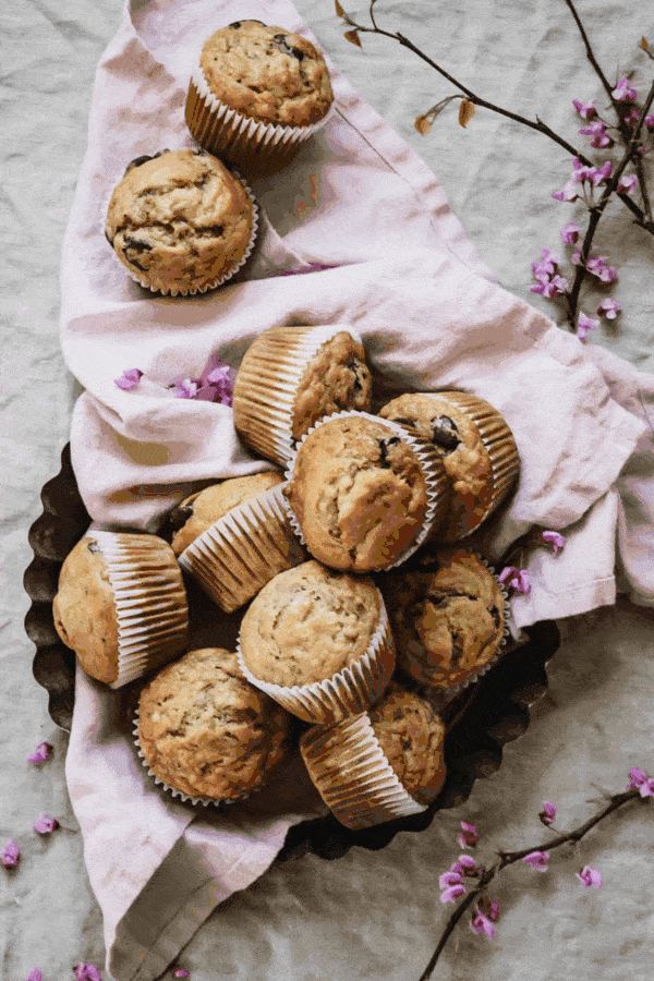 two alternating overhead shots. the first is neatly organized cookies cookies on a cookie rack set on a blue background. the second is muffins piled inside of a tart pan lined with a lilac tea towel.