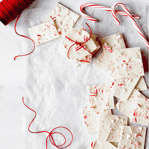 alternating images of white chocolate peppermint bark. the first image is a close up with a yellow tint. the second image is an arrangement of squares of white chocolate bark, two candy canes, and red twine.